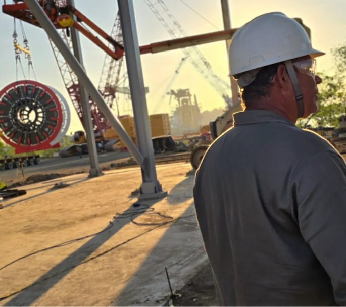 Engenheiro usando capacete de segurança em canteiro de obras com estrutura metálica sendo montada ao fundo, representando os projetos da Potência Estrutural e o compromisso com qualidade e segurança.